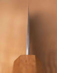 A close-up of a knife blade vertically on a wooden block against a warm beige background.