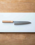 Chef's knife with wooden handle on a white cutting board over a wooden surface