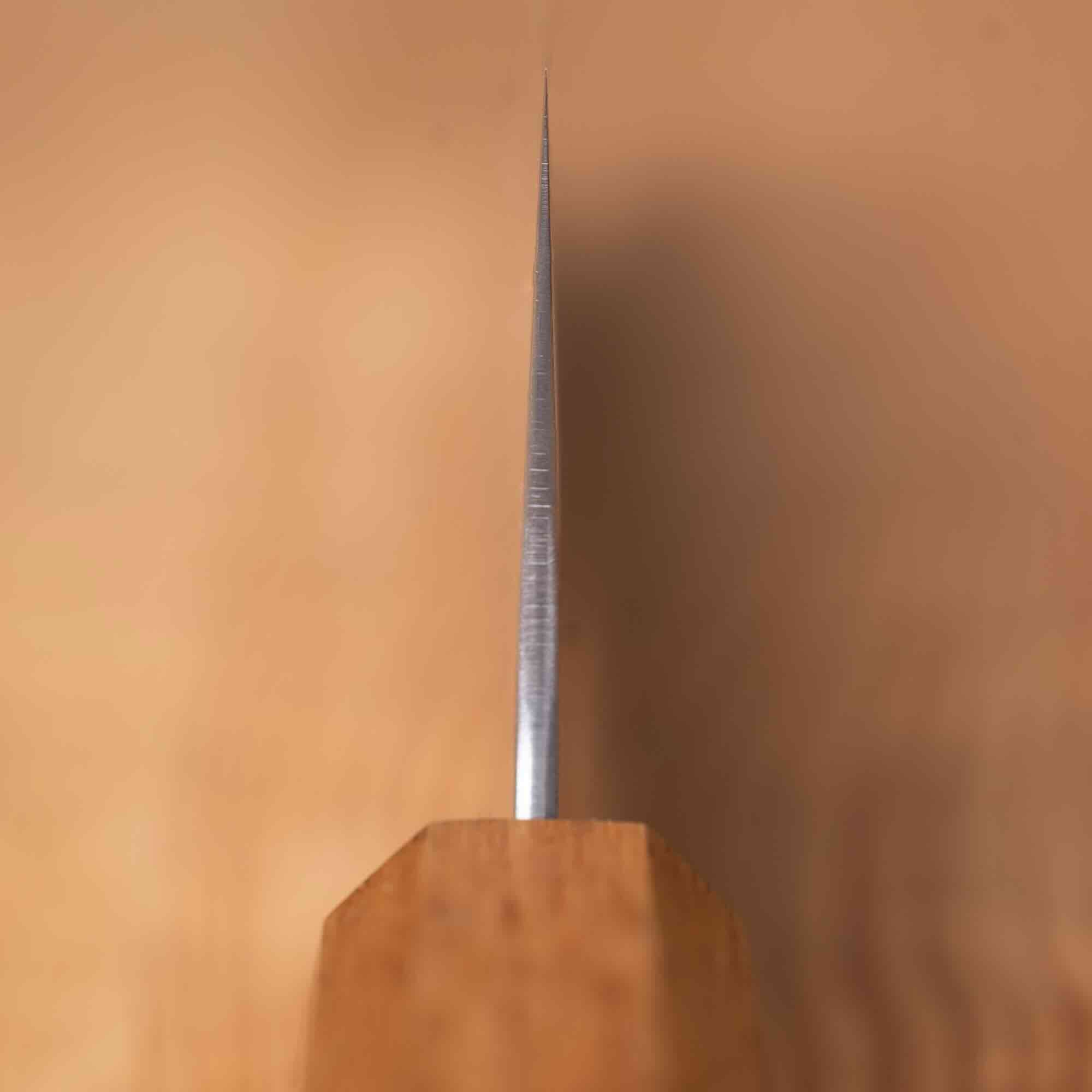 A close-up of a knife blade vertically on a wooden block against a warm beige background.