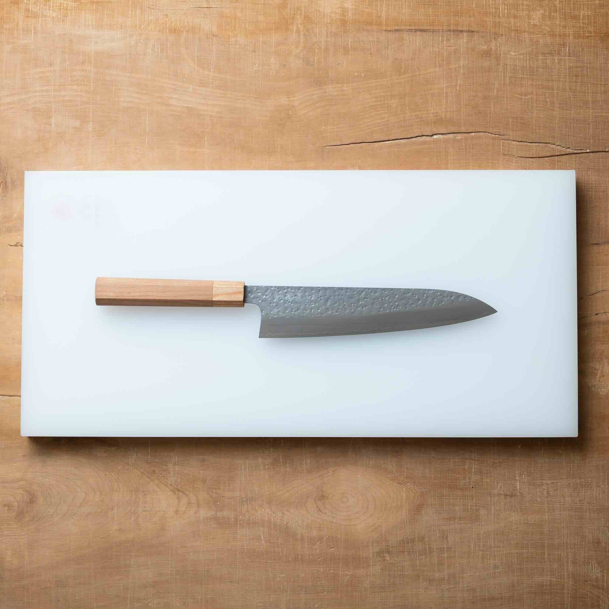 Chef's knife with wooden handle on a white cutting board over a wooden surface